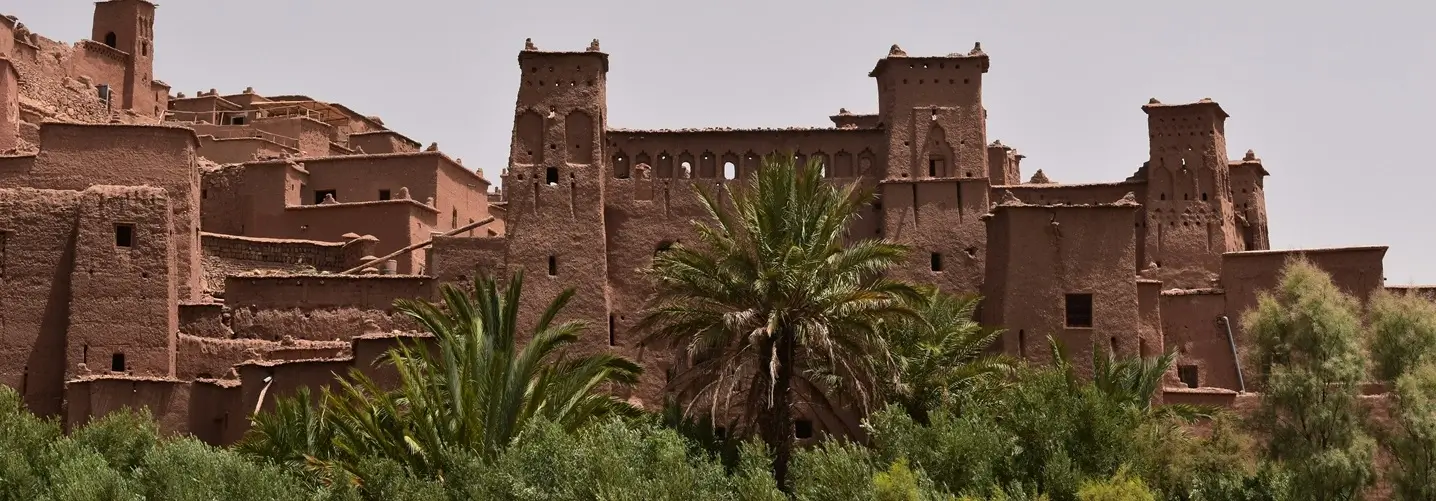 The ancient Kasbah Ait Ben Haddou with its distinctive red clay structures, framed by lush green palms, captured during a 3-day tour experience