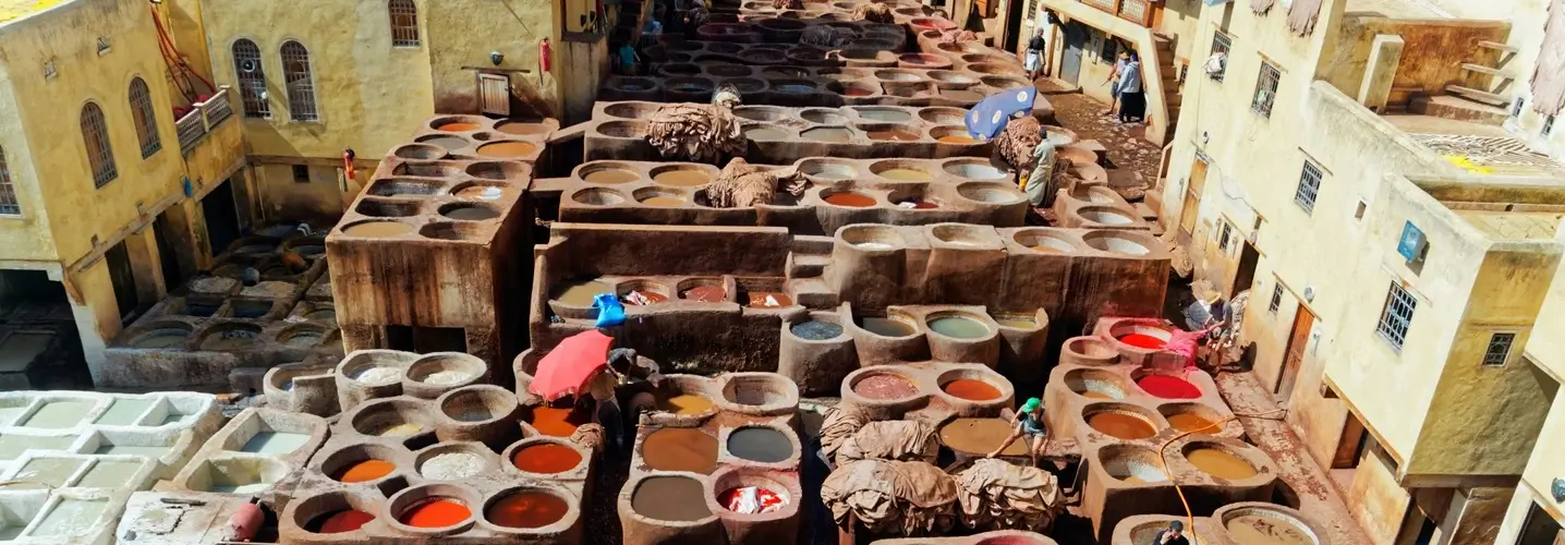 Workers laboring in the historic tanneries of Fes, surrounded by colorful dye pits, as part of the cultural experience on a 3-day tour from Fes to the desert